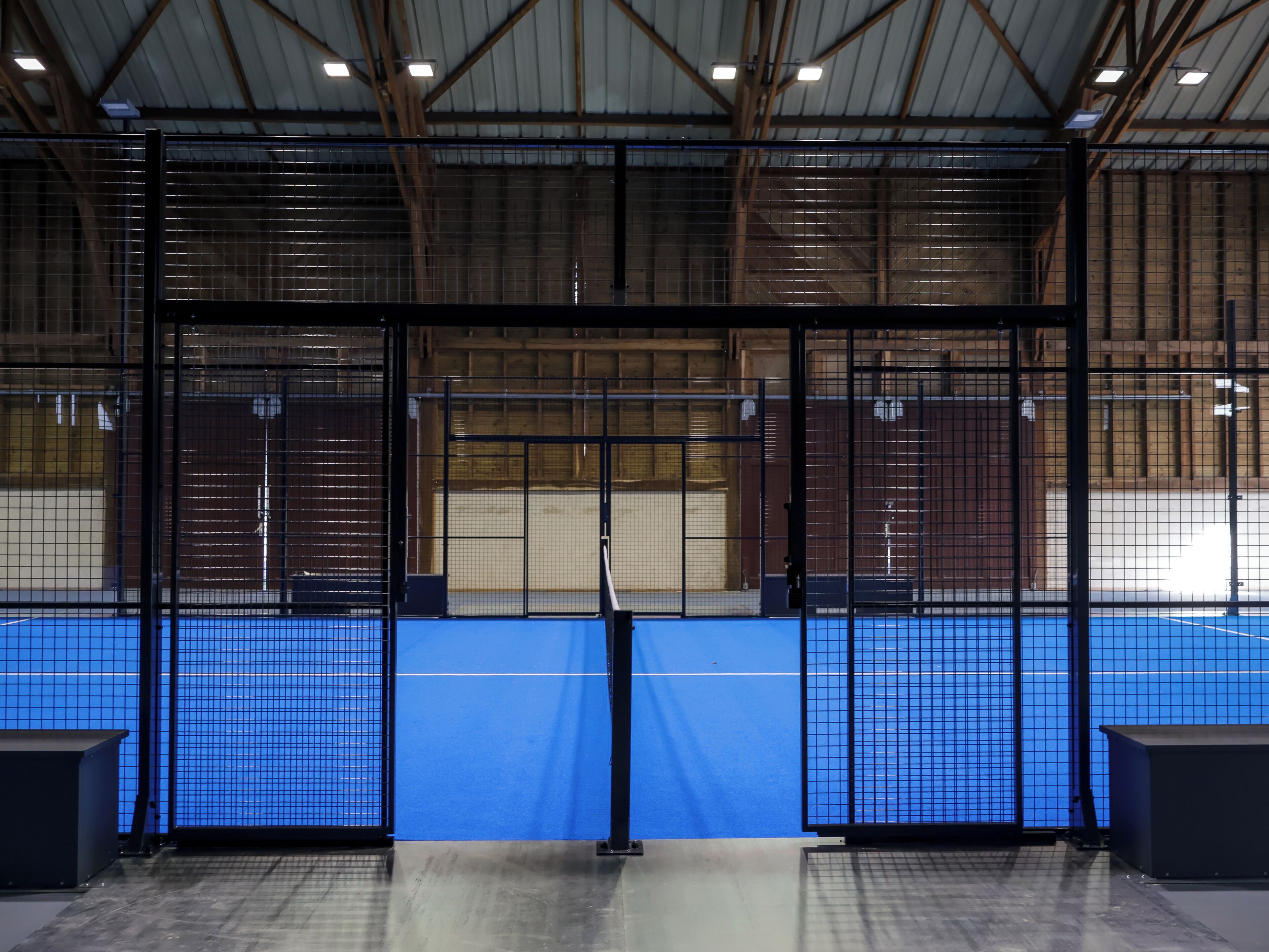 An indoor sports facility with a blue floor, metal fencing, and a high ceiling with visible beams.