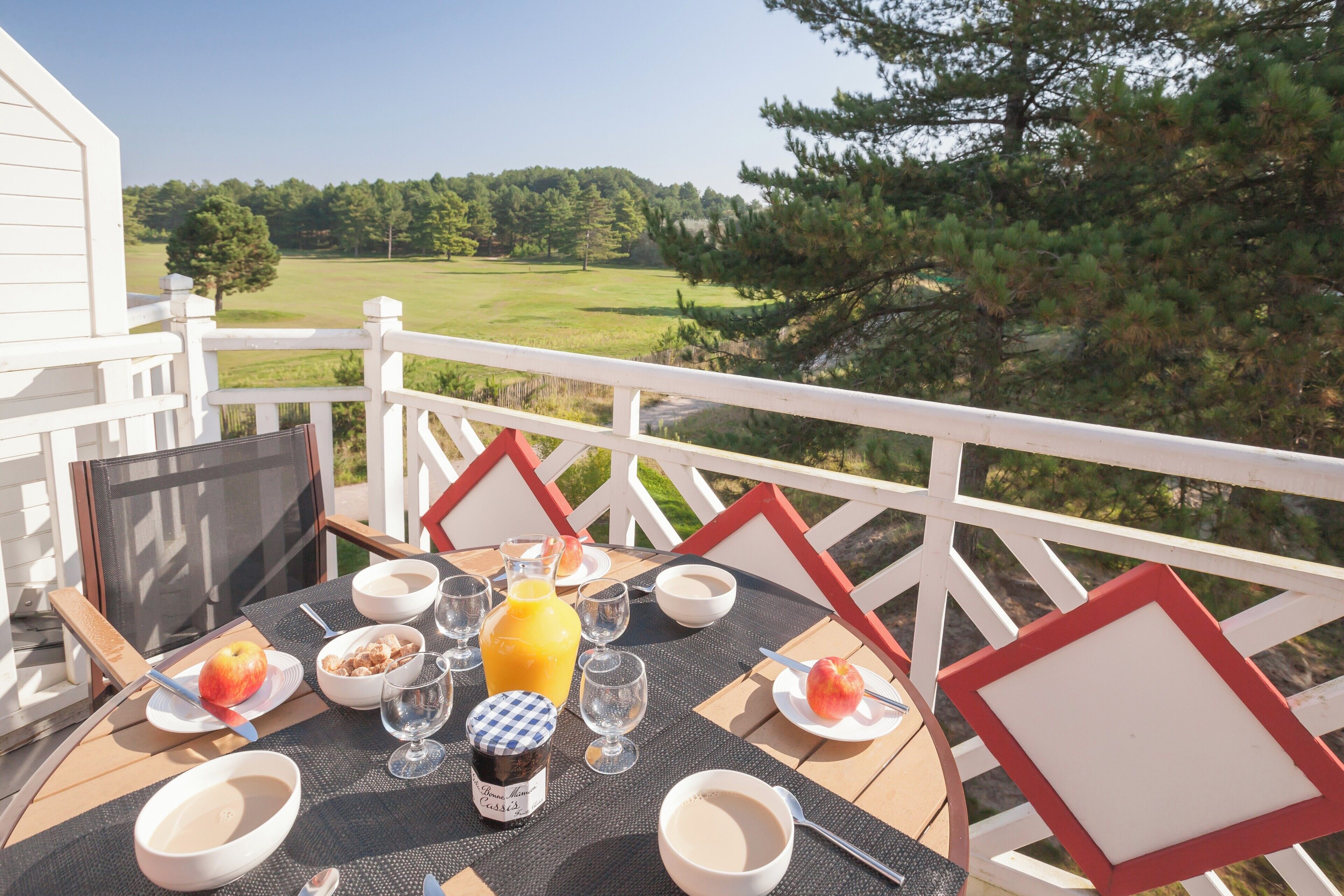 A breakfast table on a balcony with a scenic view of a golf course and trees.