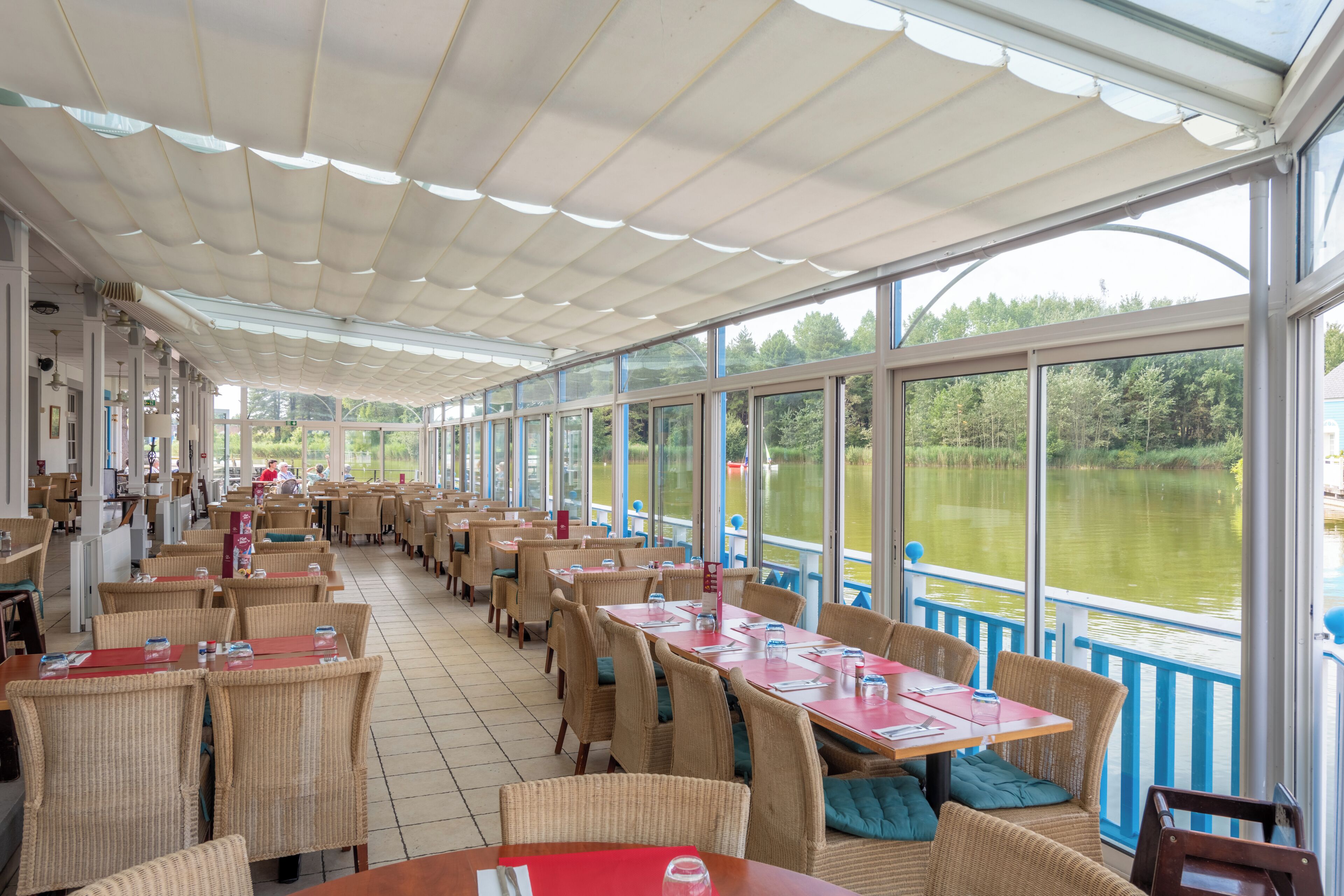 A restaurant with outdoor seating overlooking a lake, featuring wicker chairs and tables with red placemats.