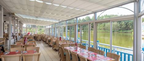 A restaurant with outdoor seating overlooking a lake, featuring wicker chairs and tables with red placemats.