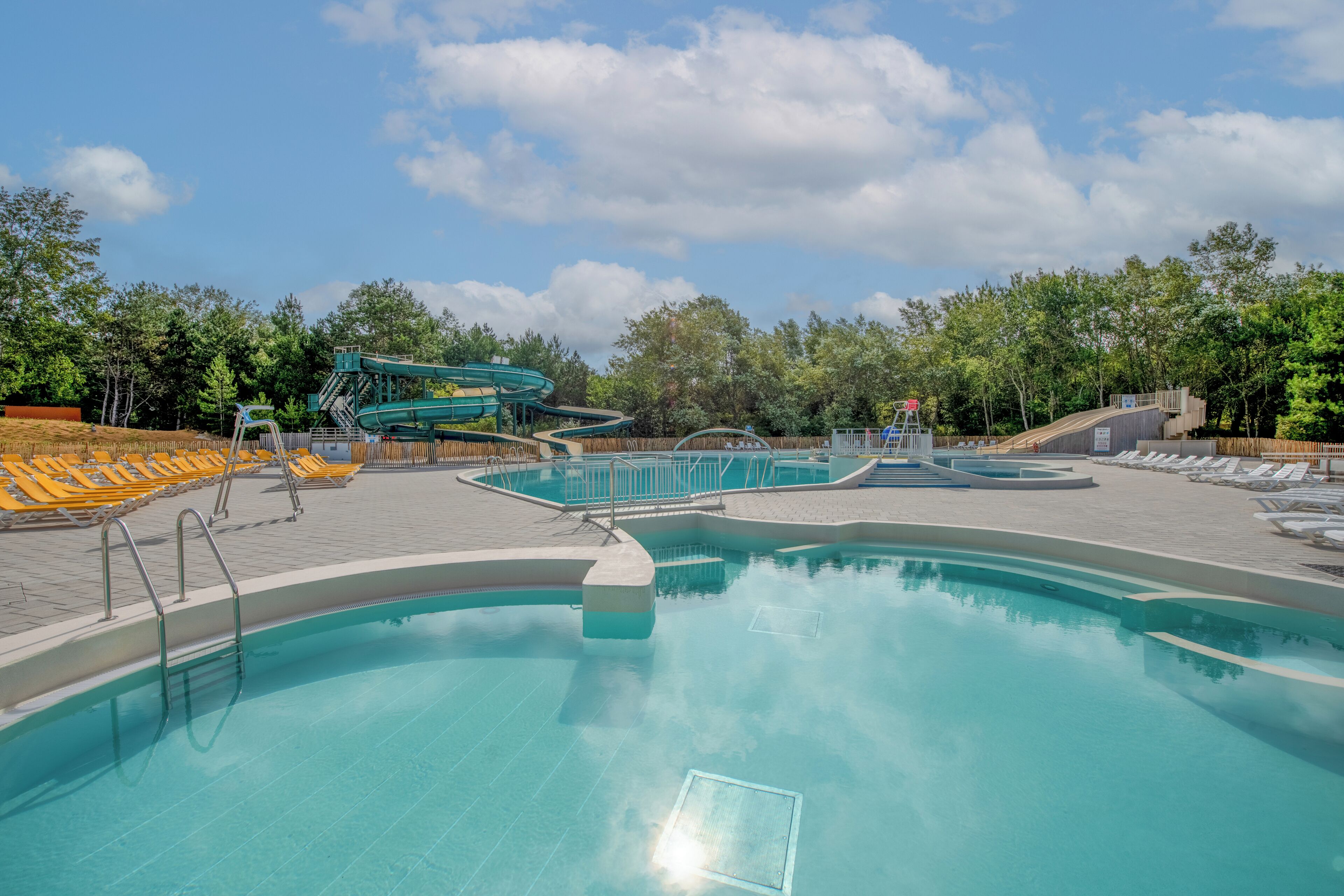 A swimming pool with a water slide, sun loungers, and a wooden deck area.