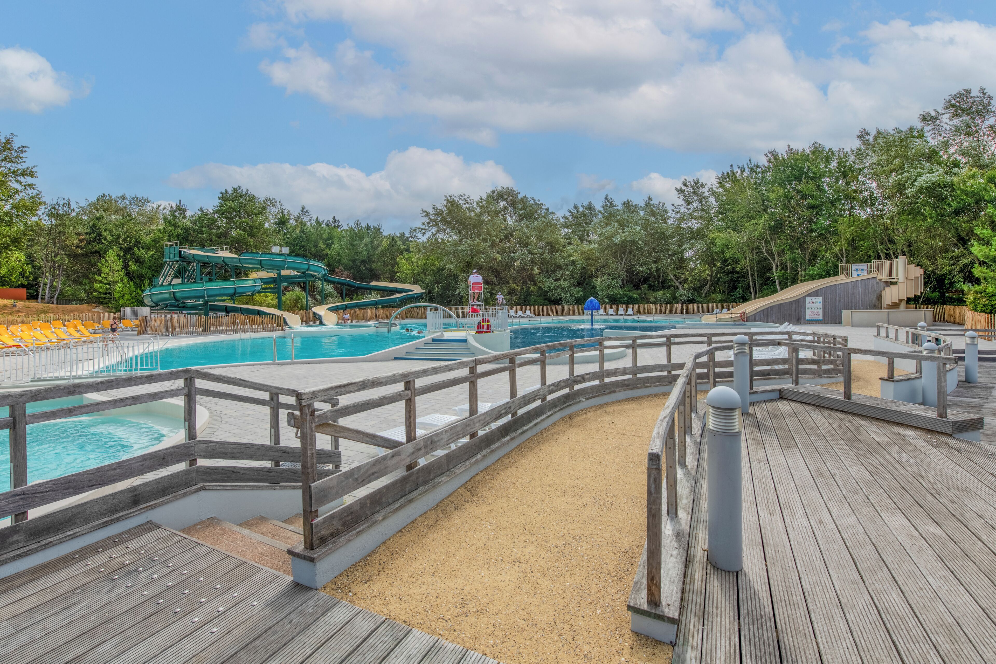 Un espace piscine doté d’une terrasse en bois, d’un toboggan et d’une tour de surveillance pour les sauveteurs.