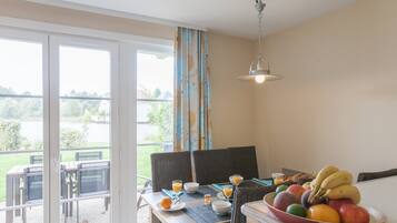 En matplats med ett bord dukat för frukost, inklusive frukt och glas för juice, med utsikt över en trädgård.