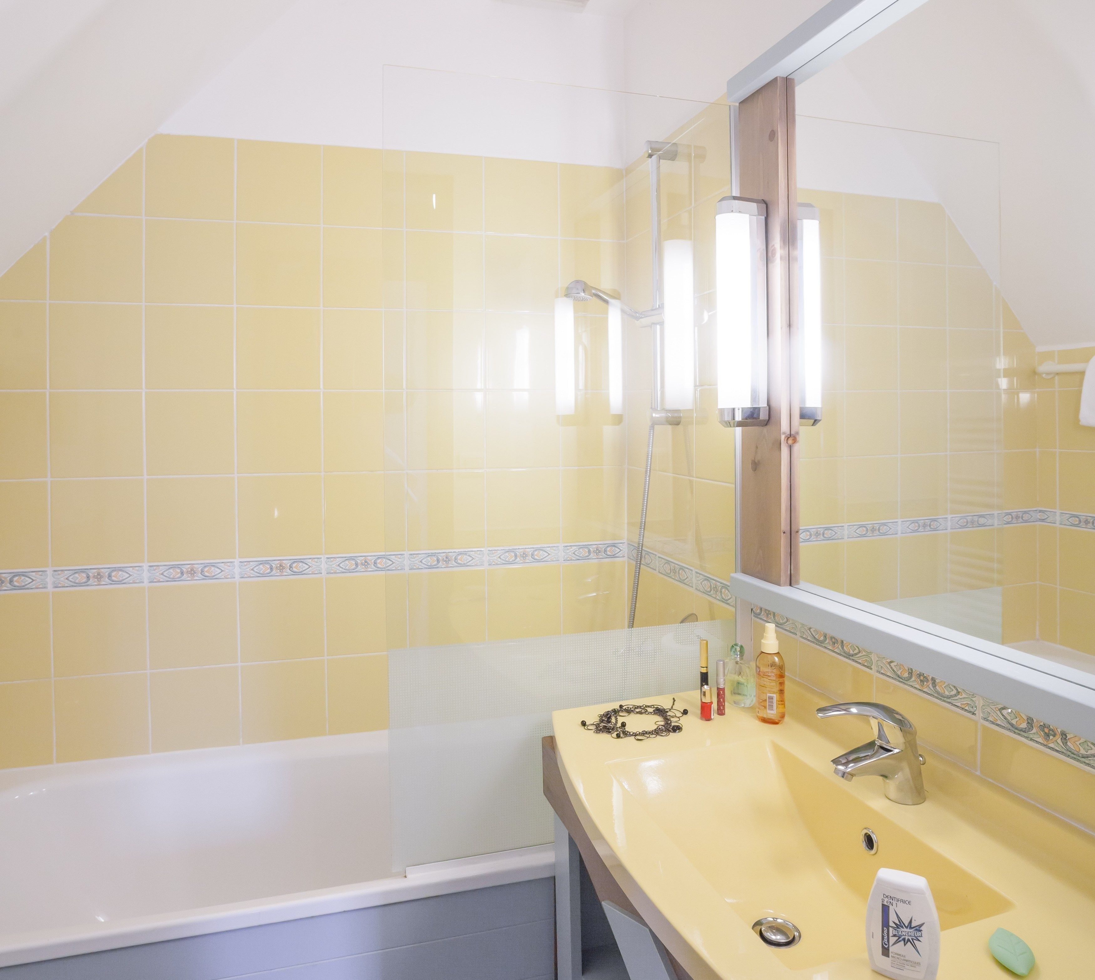 A bathroom with yellow tiles, a white bathtub, a sink with toiletries, and a mirror.
