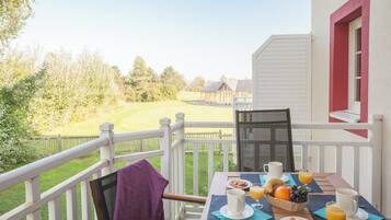 Un balcón con una mesa dispuesta para el desayuno, vistas a un campo de golf y un edificio con marcos de ventana rojos.