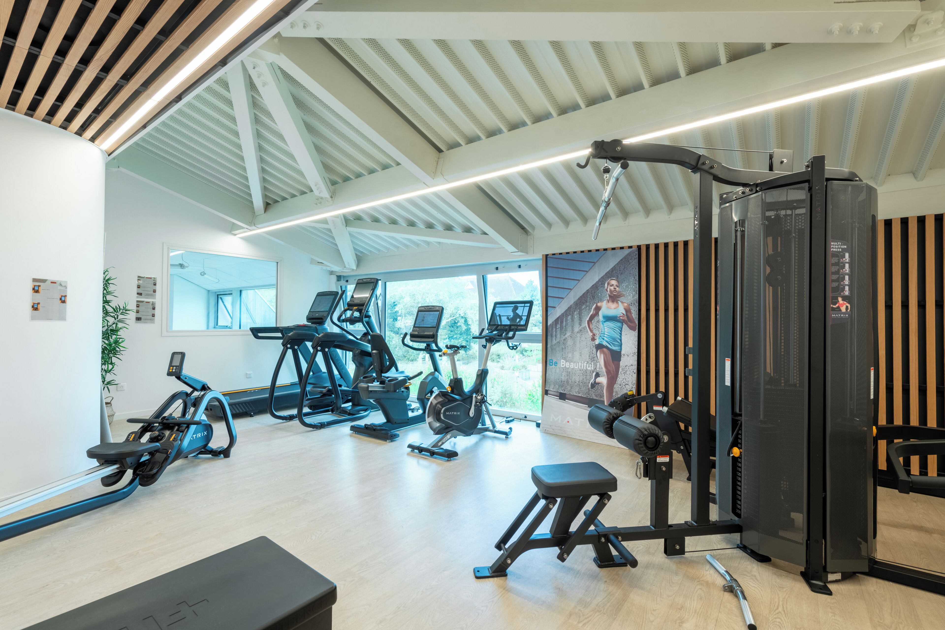 Ein Fitnessstudio mit verschiedenen Trainingsgeräten, einer Bank und einem an der Wand montierten Fernseher.