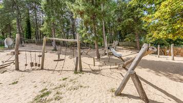 Un terrain de jeux avec des balançoires, des toboggans et des structures d’escalade, le tout entouré d’arbres.