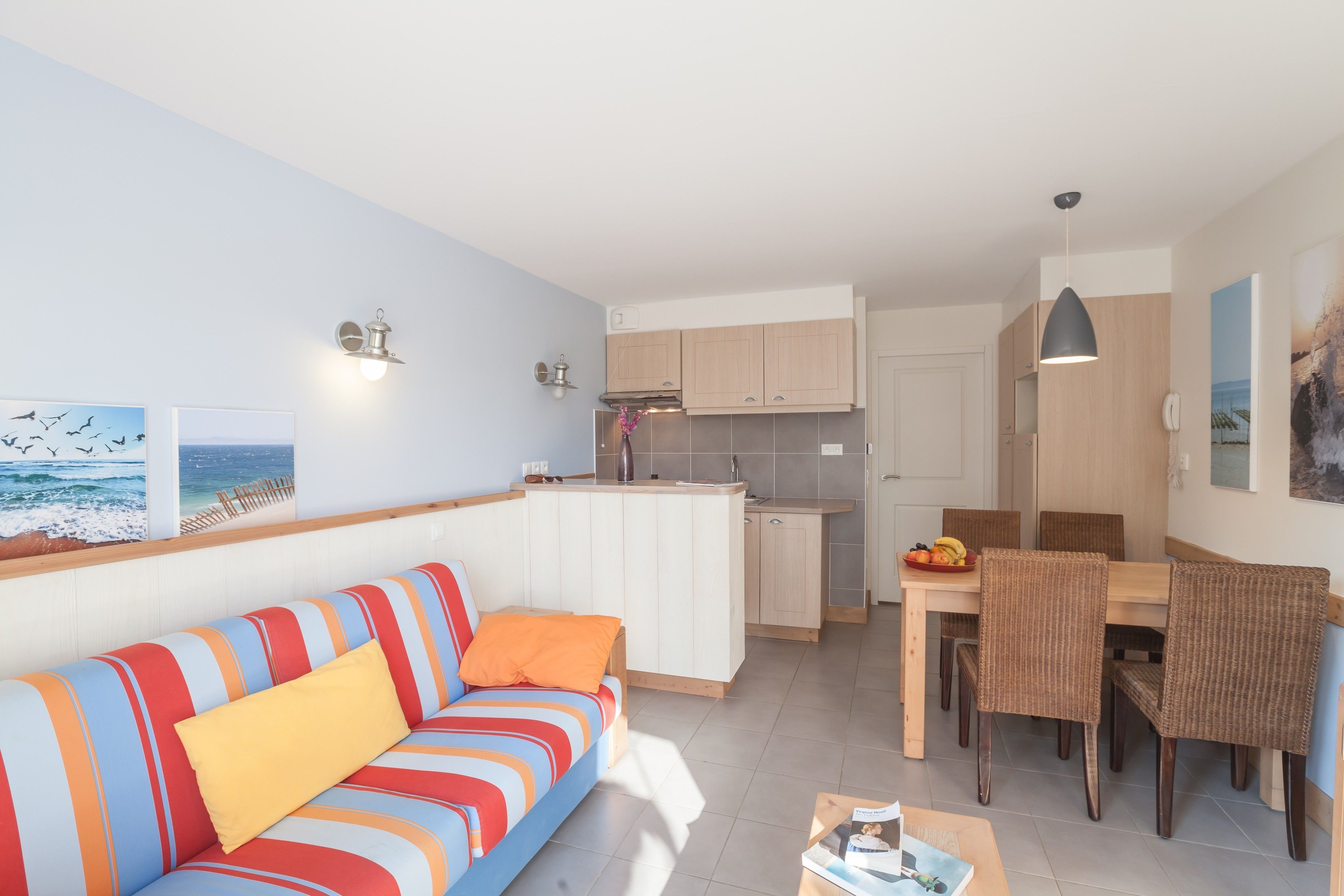 A modern living room with a striped sofa, a dining area with wicker chairs, and a kitchen with wooden cabinets.