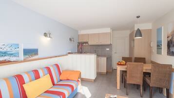 A modern living room with a striped sofa, a dining area with wicker chairs, and a kitchen with wooden cabinets.