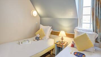 Une chambre d’hôtel avec deux lits, une table de chevet avec une lampe, un ours en peluche et une télécommande.
