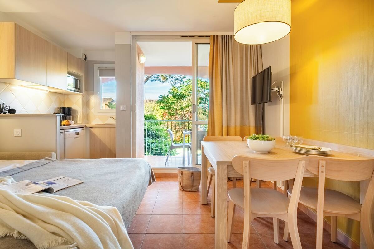 Ein Hotelzimmer mit Bett, Esstisch mit Stühlen, Wandfernseher und Balkon mit Blick ins Grüne.