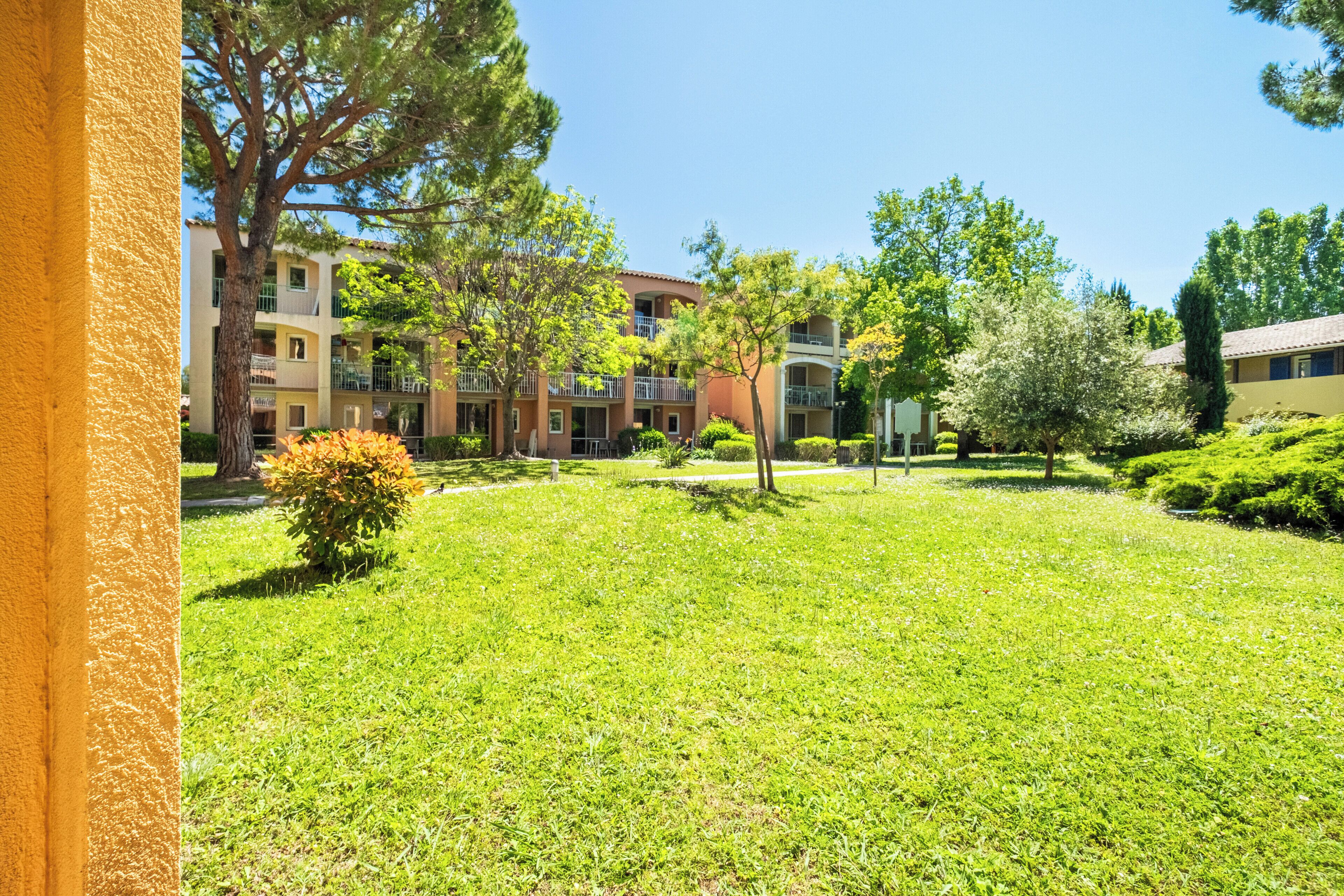 A courtyard with grass, trees, and a building with balconies.
