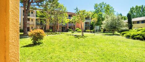 A courtyard with grass, trees, and a building with balconies.