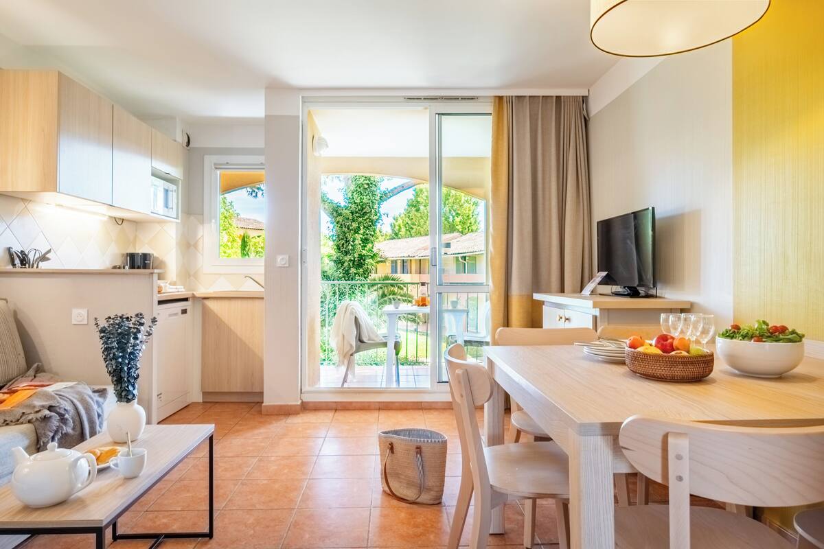 Eine moderne Küche mit Essbereich, einem Fernseher und einem Balkon mit Blick auf Grünflächen.
