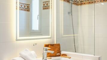 Ein Badezimmer mit weißem Waschbecken, einem Spiegel, einer Duschkabine und dekorativen Fliesen.