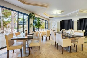 Une salle à manger d’hôtel avec des tables et des chaises, de grandes fenêtres et une vue sur l’extérieur.