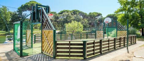 Ein Spielplatz mit Basketballkorb, Klettergerüst und umzäunter Fläche.