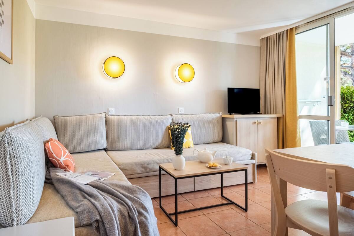 Ein modernes Wohnzimmer mit einer Couch, einem Couchtisch, einem Fernseher und einem Fenster mit Vorhängen.