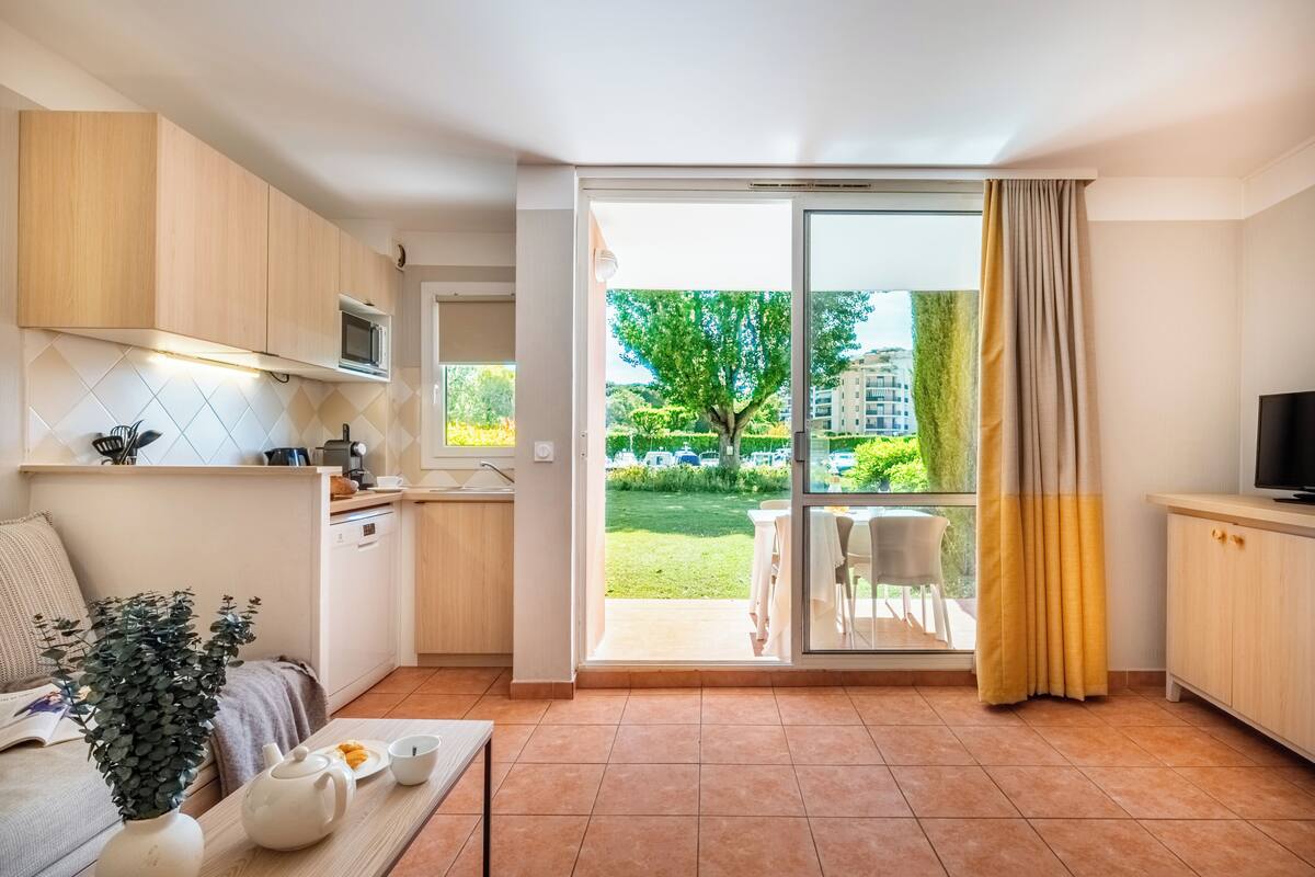 Eine moderne Küche mit Mikrowelle, ein Essbereich mit Tisch und Stühlen sowie eine Glastür, die zu einem Außenbereich mit Blick auf Grünflächen und Gebäude führt.