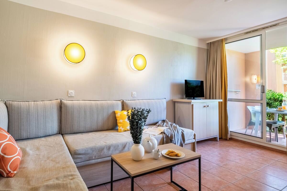 Ein modernes Wohnzimmer mit einer Couch, einem Couchtisch, einem Fernseher und einem Balkon mit Tisch und Stühlen.