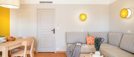 Una sala de estar moderna con un sofá, una mesa de comedor con sillas, una mesita de centro con una tetera y una cesta de frutas.
