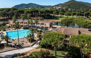 Un hotel con piscina, varias construcciones y abundante vegetación alrededor.