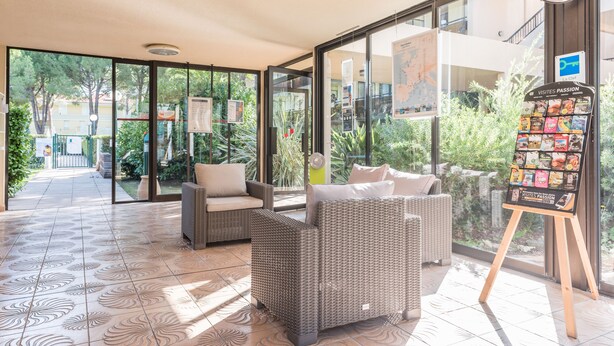 A spacious lobby with wicker furniture, a map display, and a signboard with travel information. - Pierre & Vacances Résidence Les Jardins Ombragés (Mandelieu-La-Napoule)