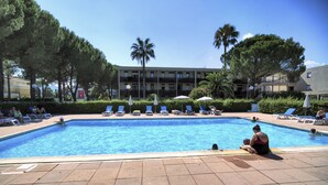 A swimming pool with lounge chairs and umbrellas, surrounded by trees and buildings. - Pierre & Vacances Résidence Les Jardins Ombragés (Mandelieu-La-Napoule)
