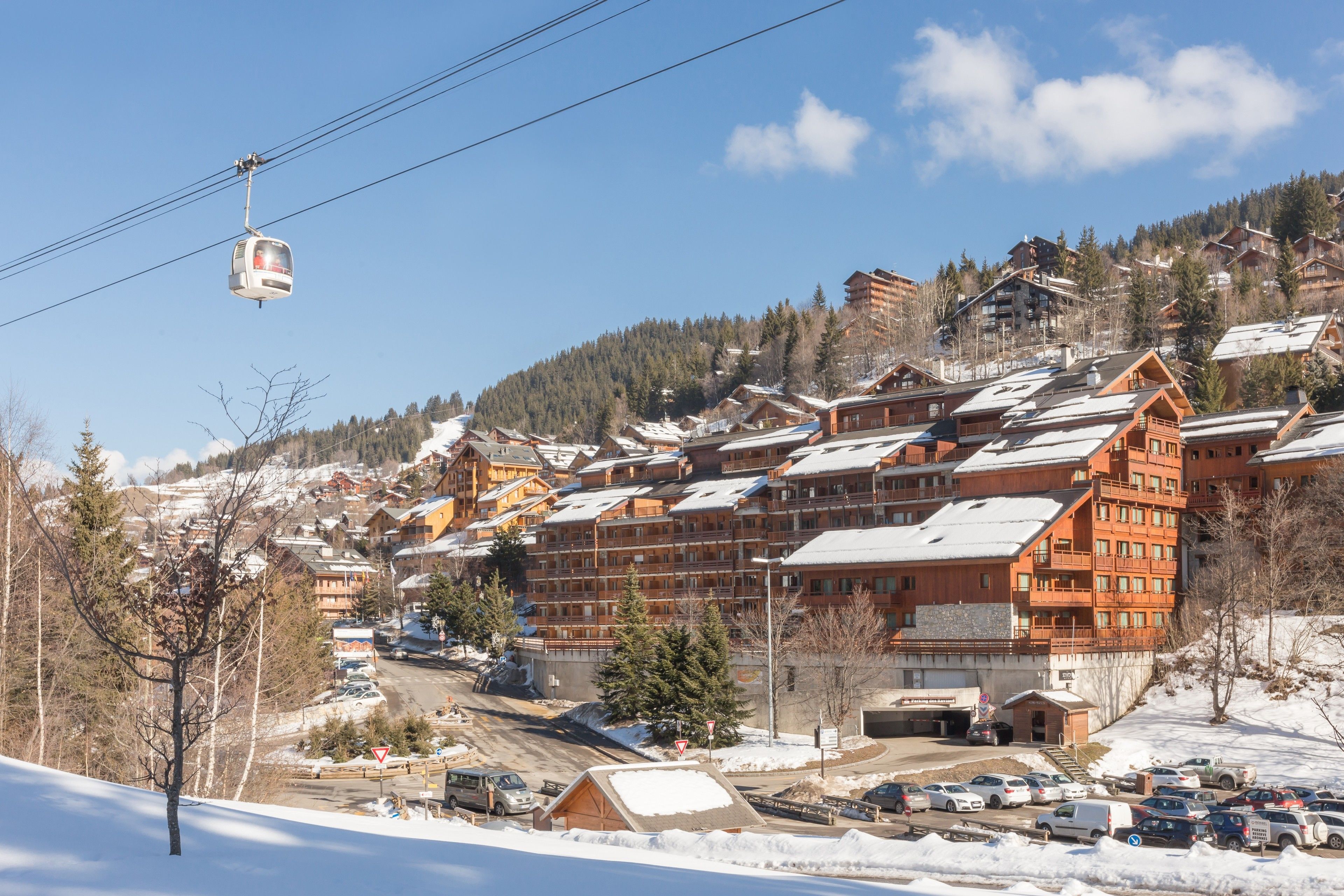A ski resort with wooden buildings, a cable car, and a parking area.
