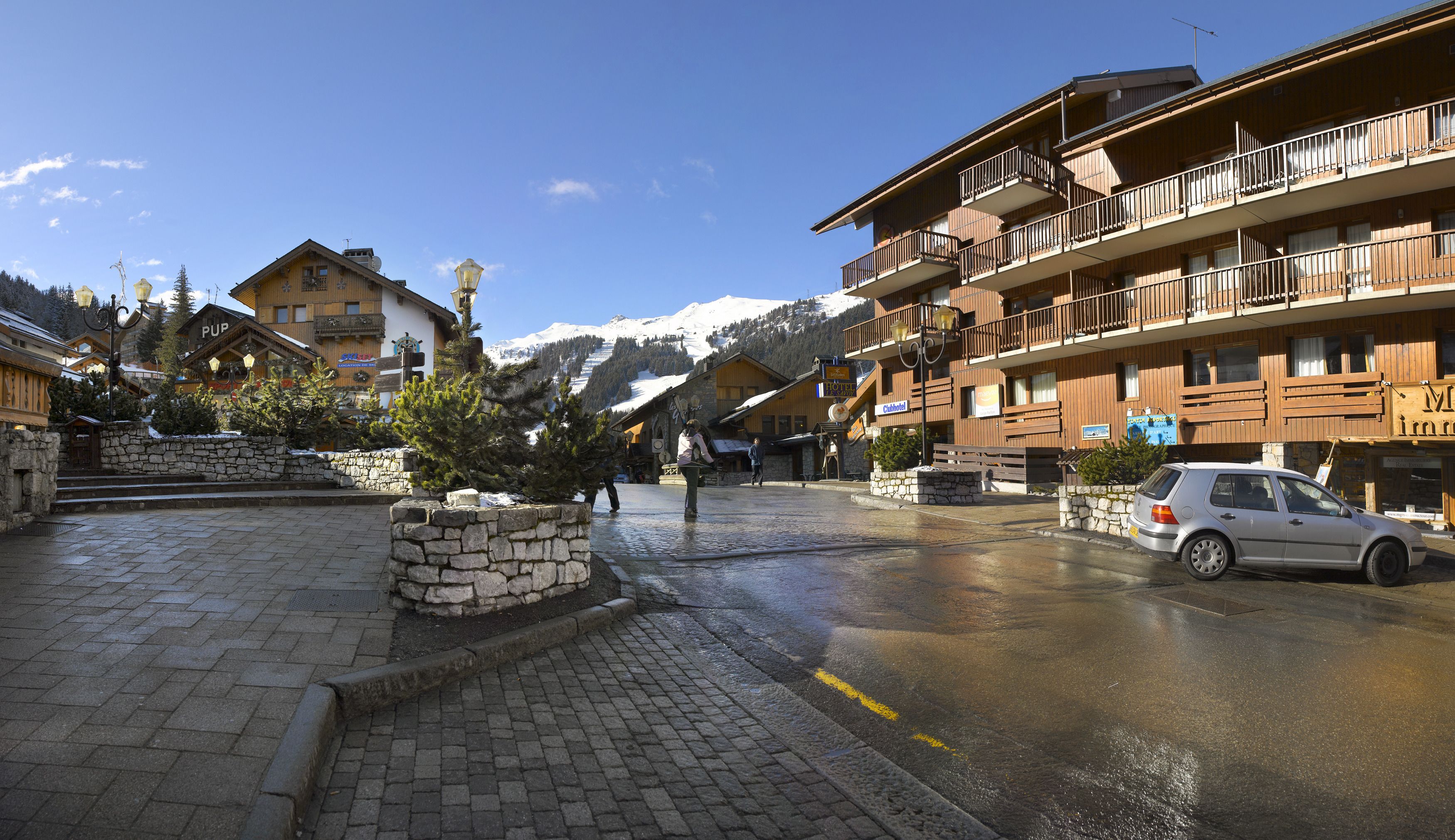 A hotel with a stone facade, wooden balconies, and a view of snow-capped mountains.
