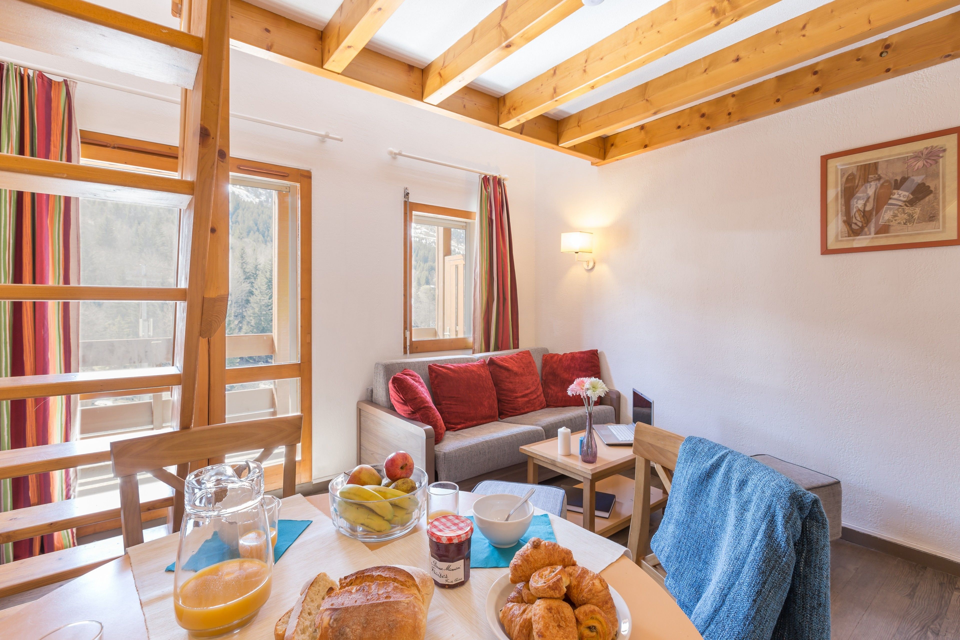 Una habitación acogedora con una mesa de comedor dispuesta para el desayuno, un sofá y una ventana con cortinas.