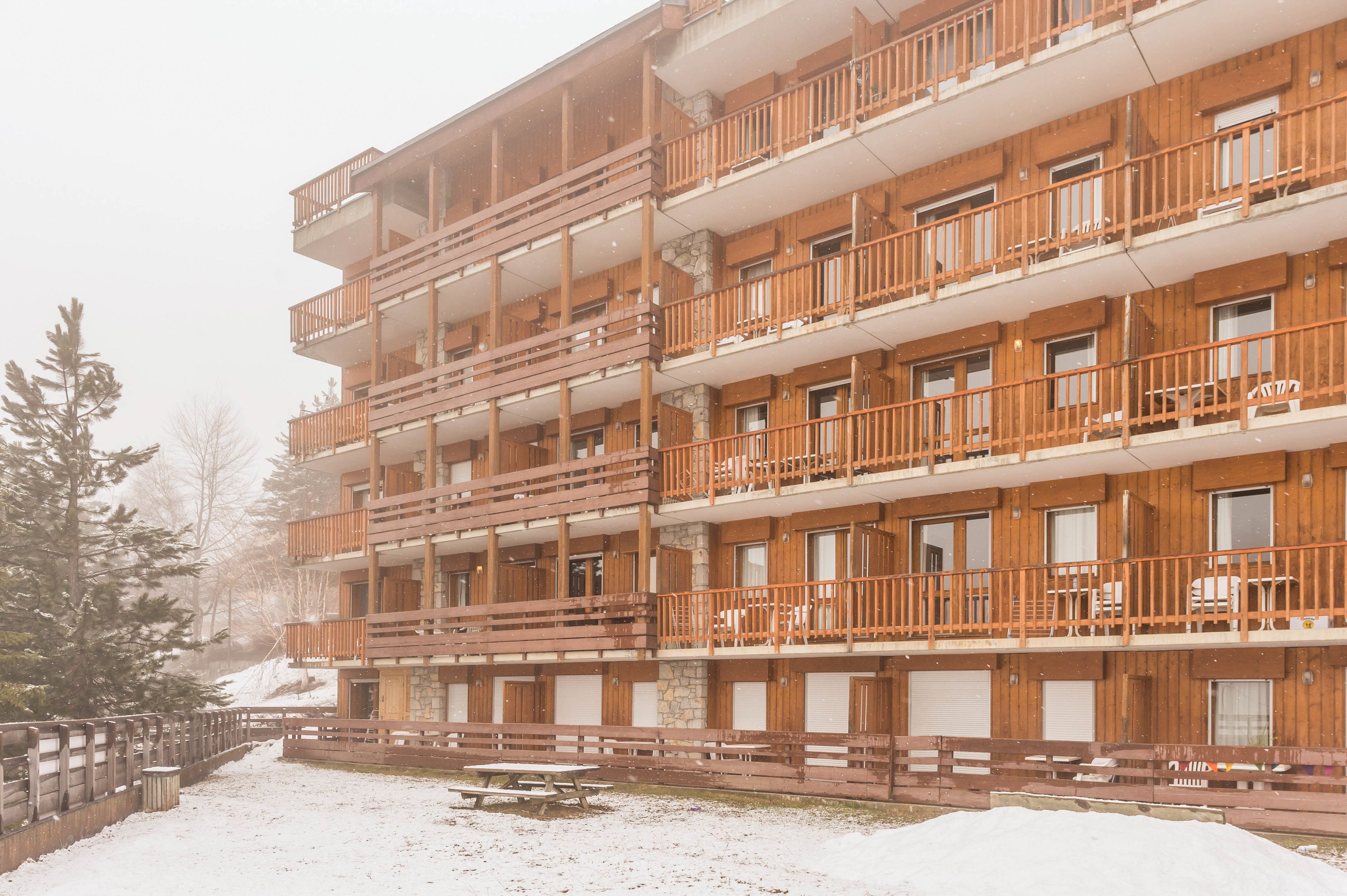 Un bâtiment en bois à plusieurs étages, doté de balcons, avec un sol enneig é et une clôture en bois.