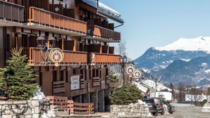 A multi-story wooden building with balconies, a stone wall, and a sign indicating it is a ski resort. - Résidence Pierre & Vacances Les Ravines (Les Allues)