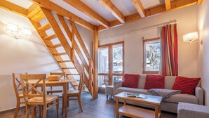 A cozy living room with wooden furniture, a sofa with red cushions, and a dining area with a table and chairs. - Résidence Pierre & Vacances Les Ravines (Les Allues)