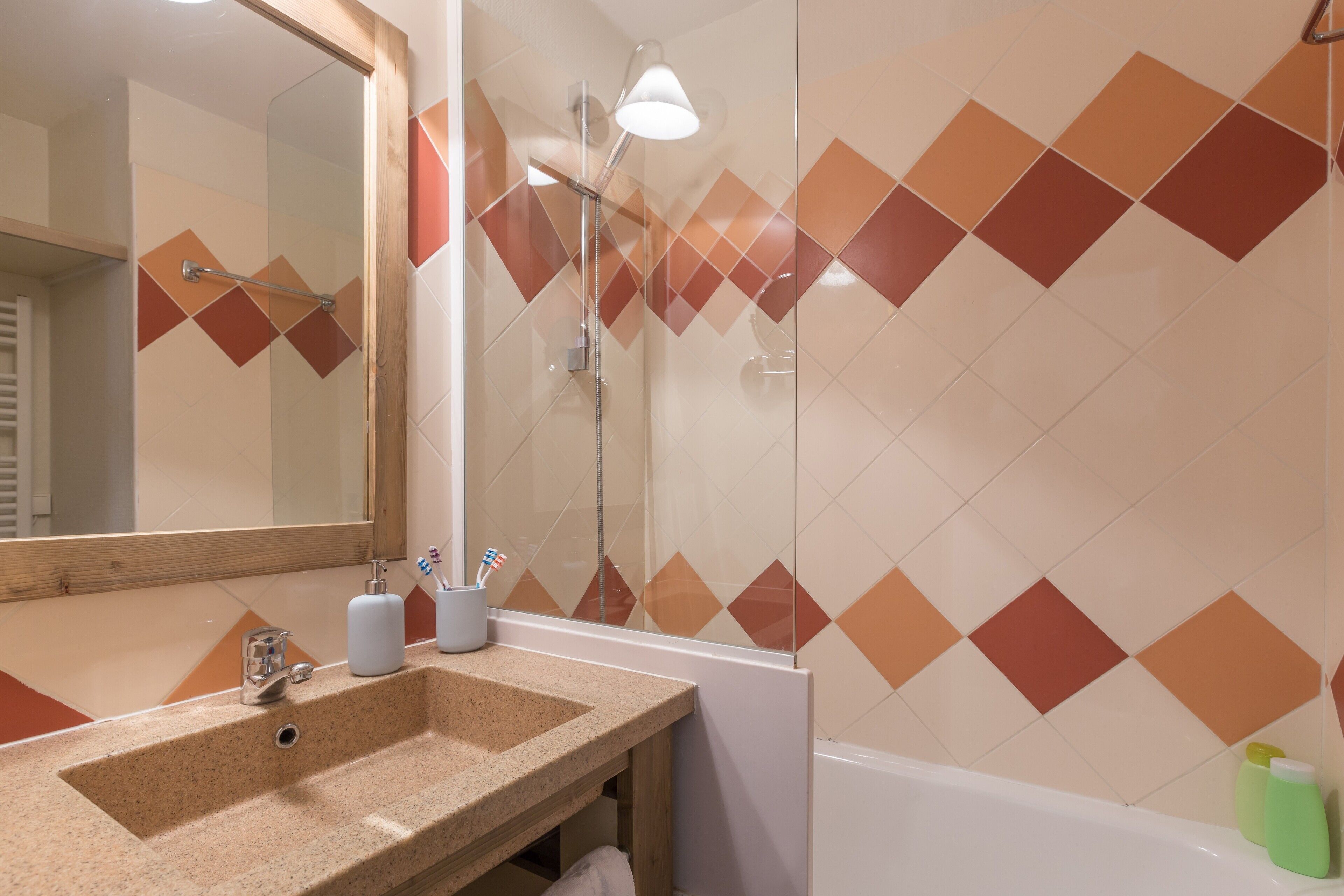 A bathroom with a sink, mirror, shower, and tiled walls.