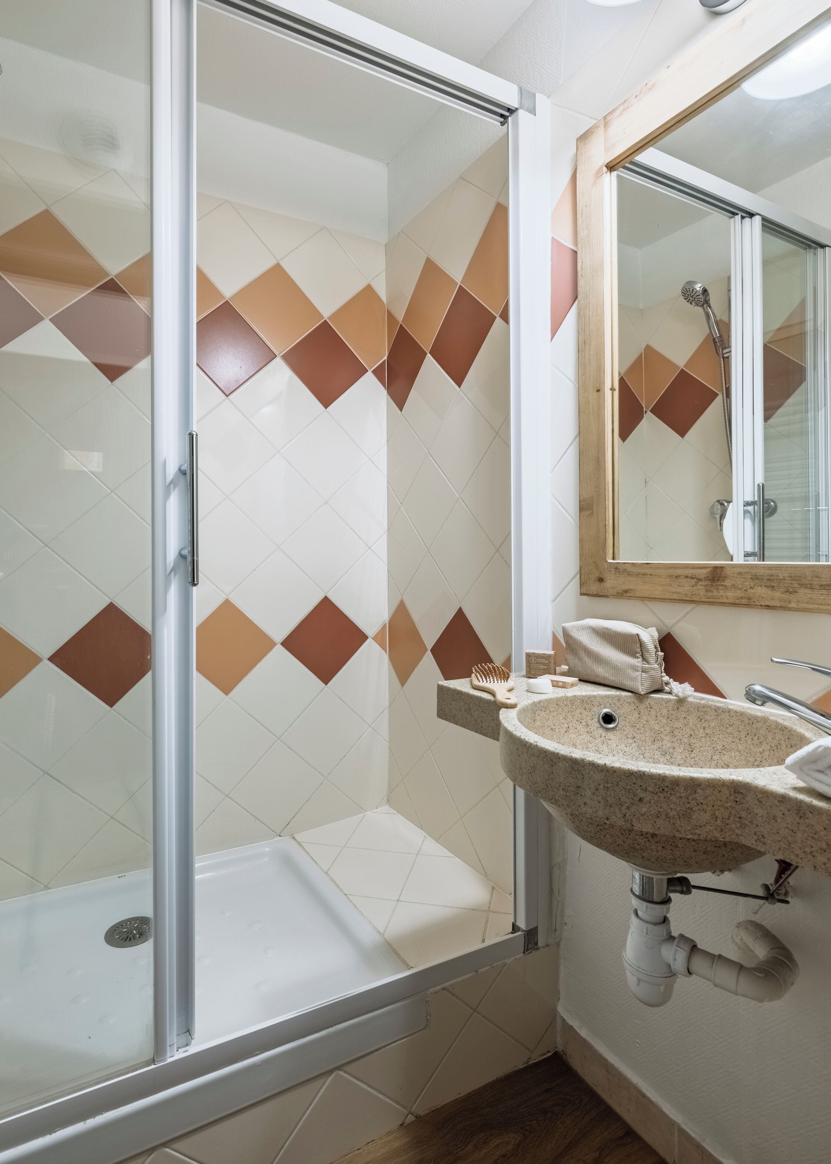A bathroom with a glass shower enclosure, a sink with a mirror, and a tiled wall with a diamond pattern.
