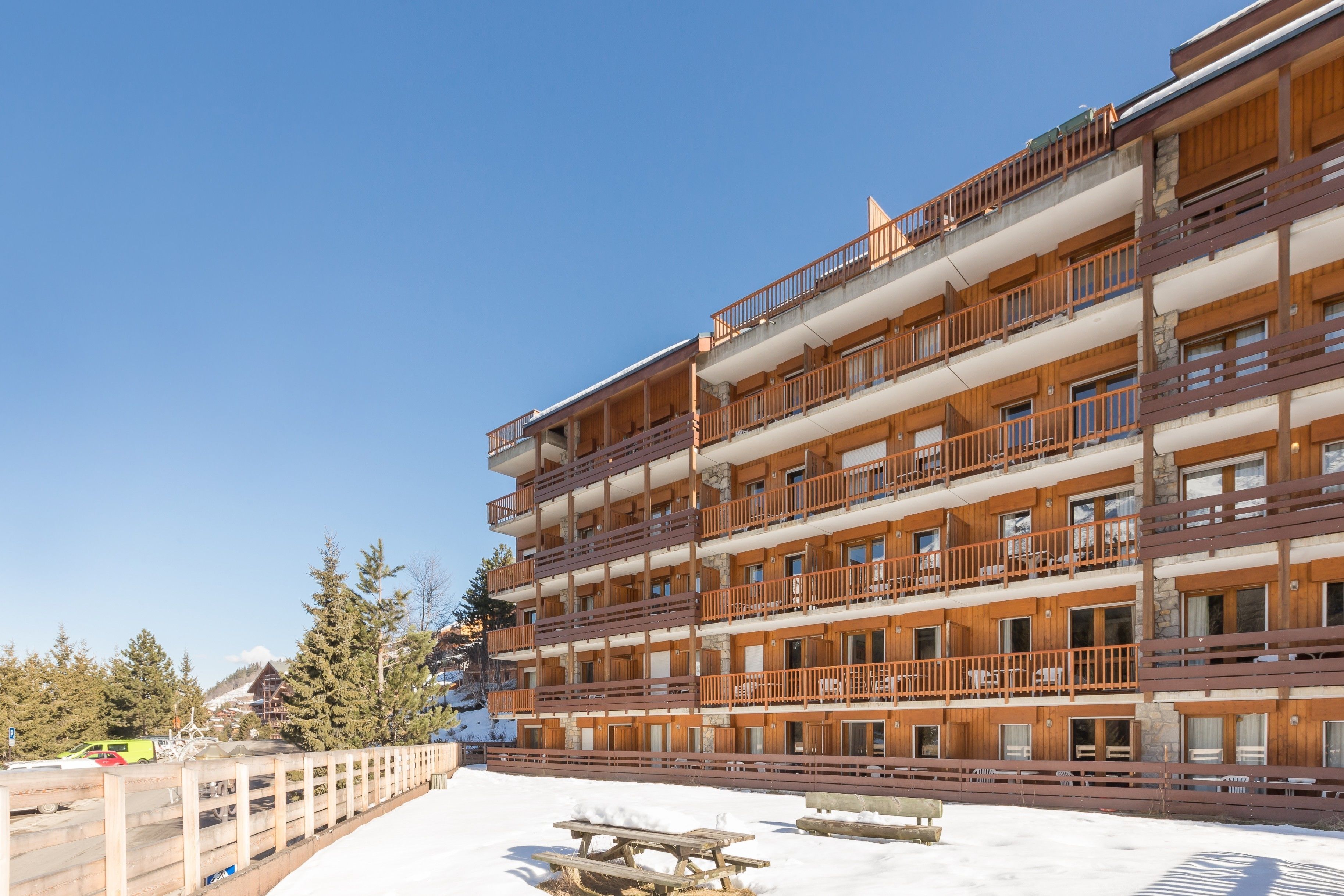 Een meerlaags hotel met balkons, een houten gevel en een besneeuwde grond.