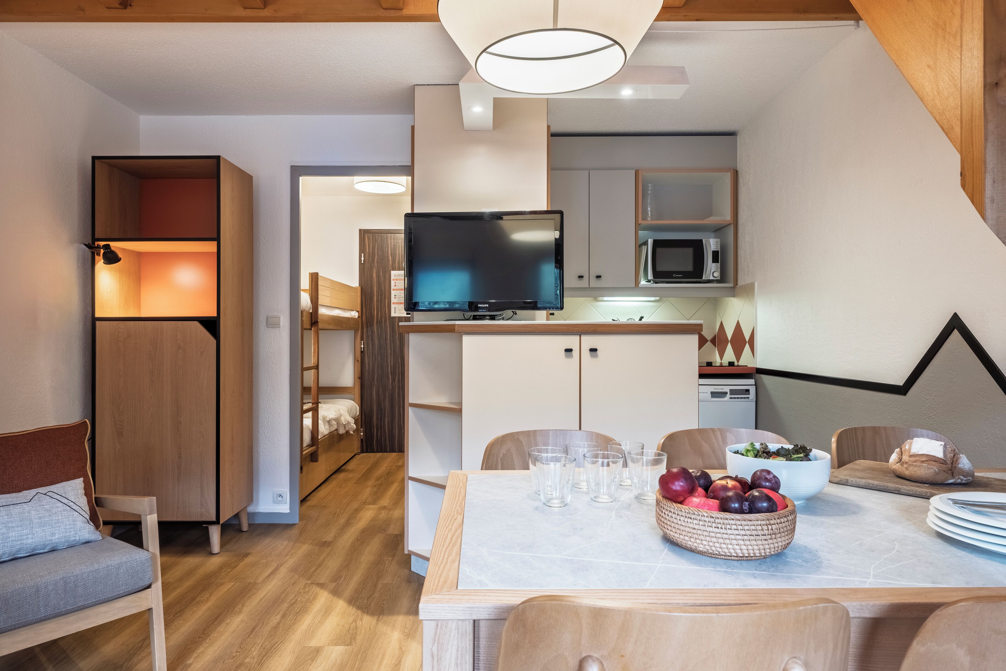 Une cuisine moderne équipée d’un téléviseur à écran plat, de meubles en bois et d’un coin repas avec une table dressée pour deux personnes.