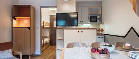 Une cuisine moderne équipée d’un téléviseur à écran plat, de meubles en bois et d’un coin repas avec une table dressée pour deux personnes.