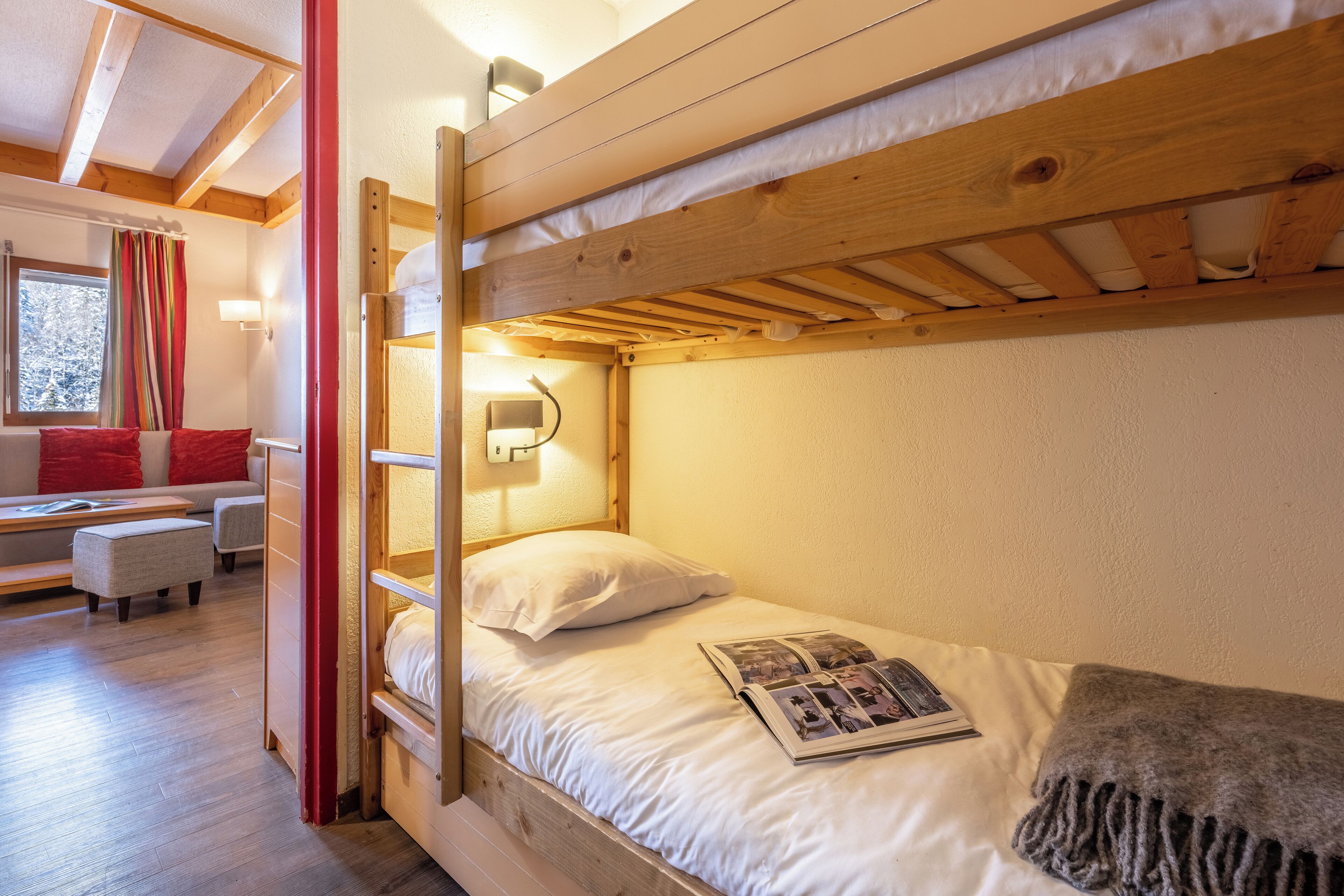 Una cama litera con una revista en la cama inferior, una mesita de noche y una ventana con cortinas.
