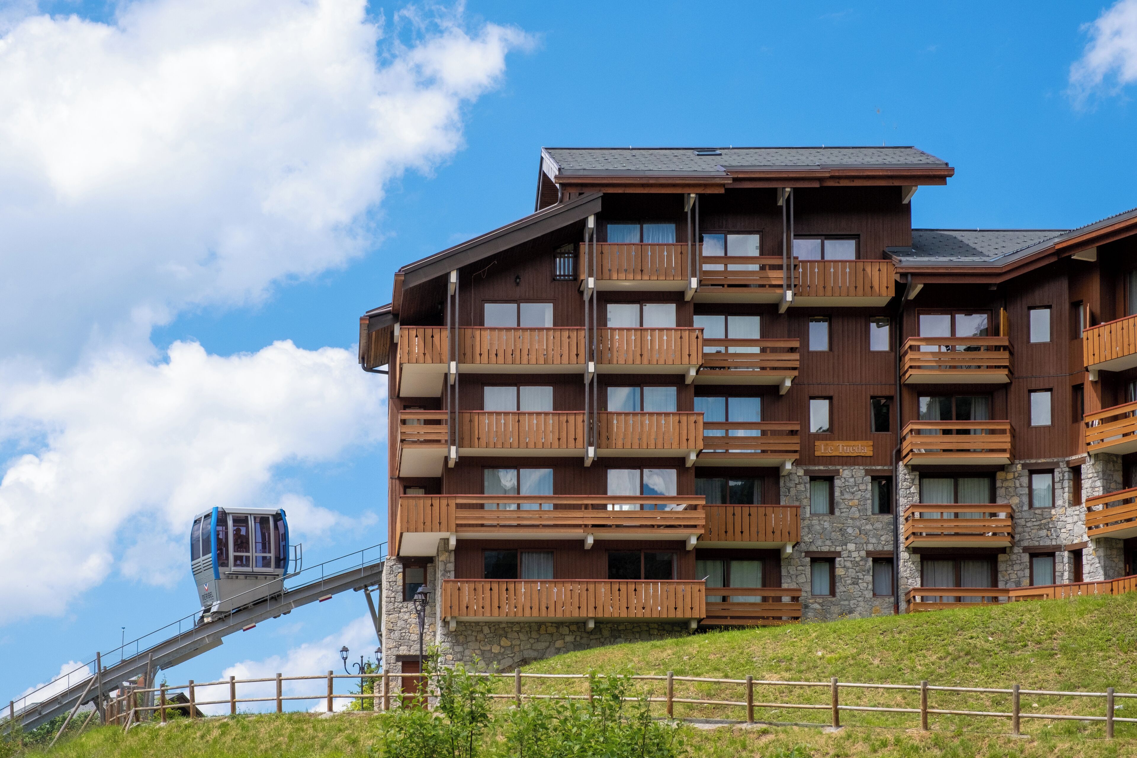 Un hotel de varios pisos con balcones, un teleférico y fachada de piedra.