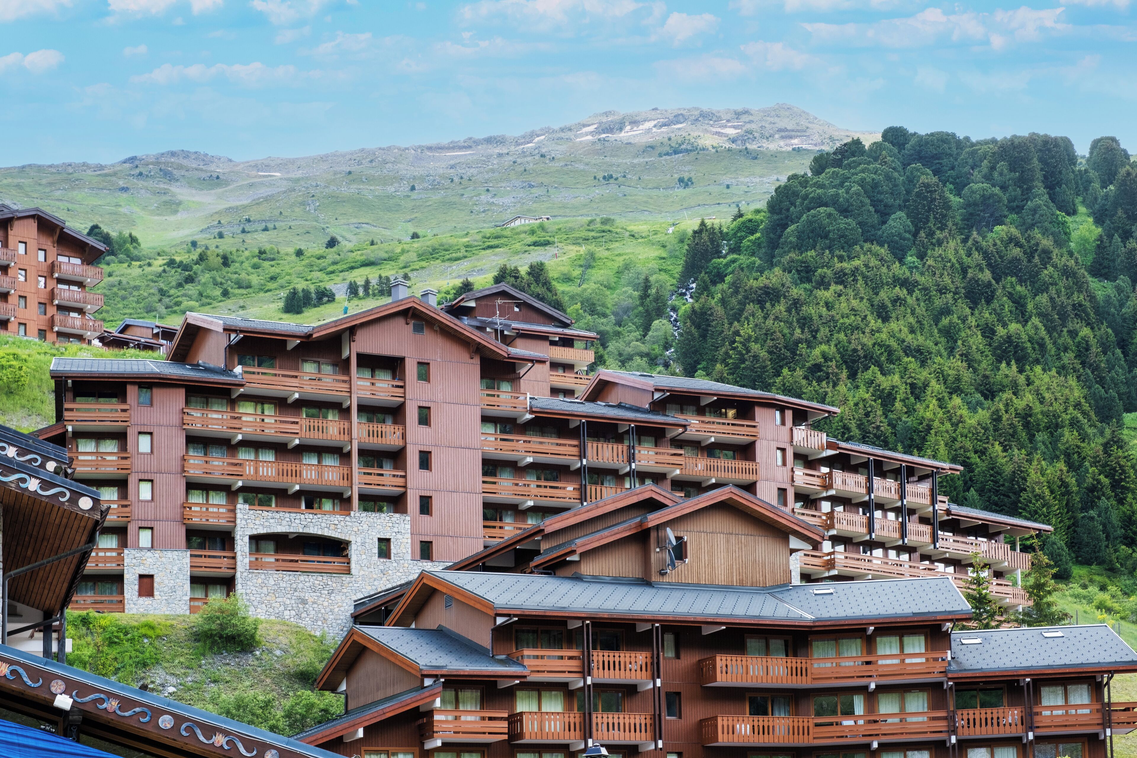 Ein mehrstöckiges Hotel mit Balkonen vor der Kulisse grüner Hügel und eines klaren Himmels.