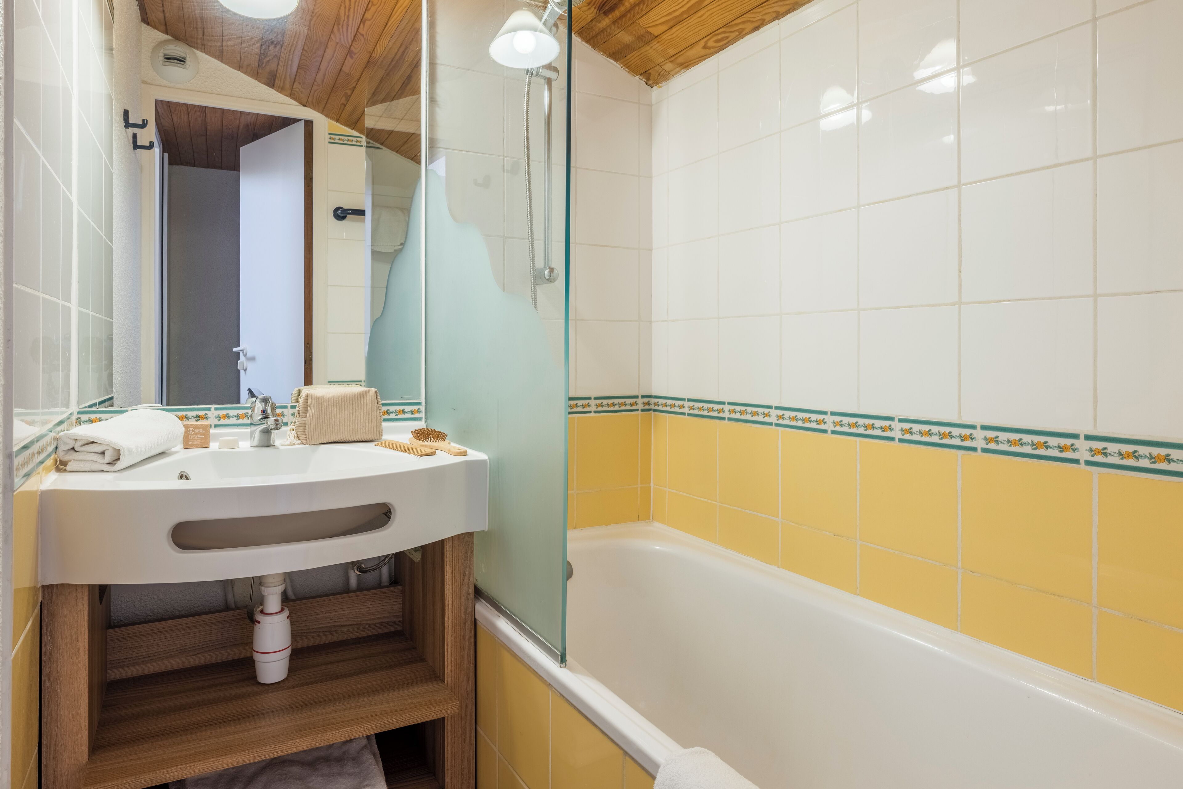 A bathroom with a wooden vanity, a sink, a mirror, a shower, and yellow-tiled walls.