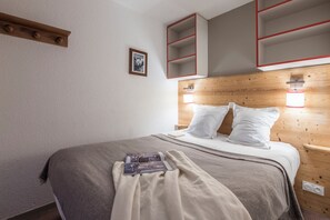 Un llit ben arrenjat amb llençols i almoadines grisos, un quadre emmarcat a la paret i prestatges integrats amb vores vermelles.