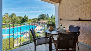 Un balcón con vista a una piscina, mesa de comedor, sillas y pared con textura.