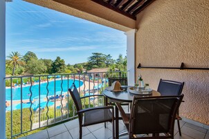 Un balcón con vista a una piscina, mesa de comedor, sillas y pared con textura.