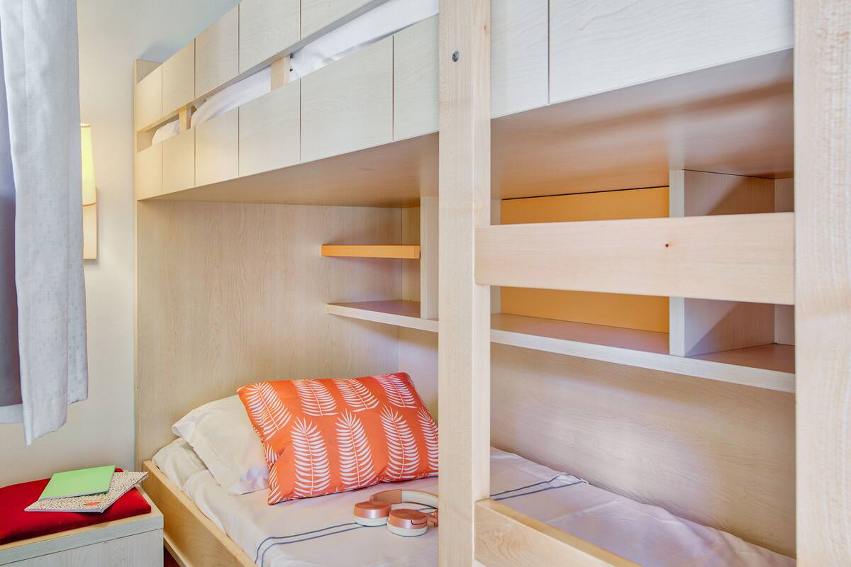 A bunk bed room with a wooden headboard, a nightstand with a red cloth, and a pillow with an orange leaf pattern.