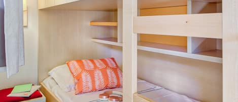 Habitación con literas, cabecera de madera, mesita de noche con un paño rojo y almohada con estampado de hojas naranjas.