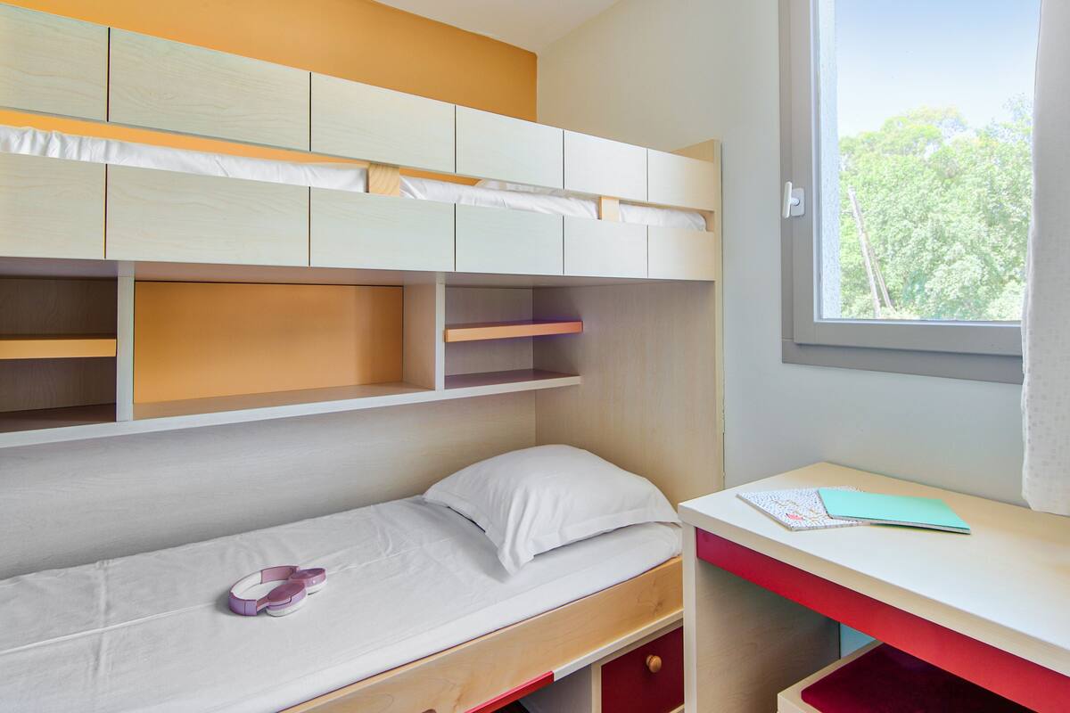 A bedroom with a bunk bed, a desk, and a window.