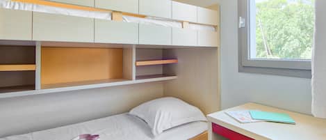 A bedroom with a bunk bed, a desk, and a window.
